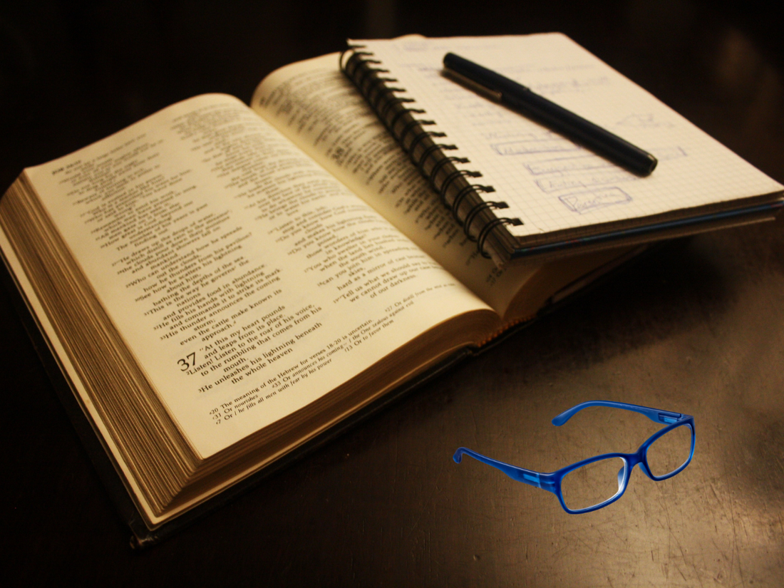 Close-up of open Bible with handwritten notes and a pen & reading glasses