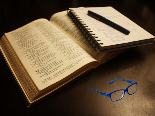 Close-up of open Bible with handwritten notes and a pen & reading glasses