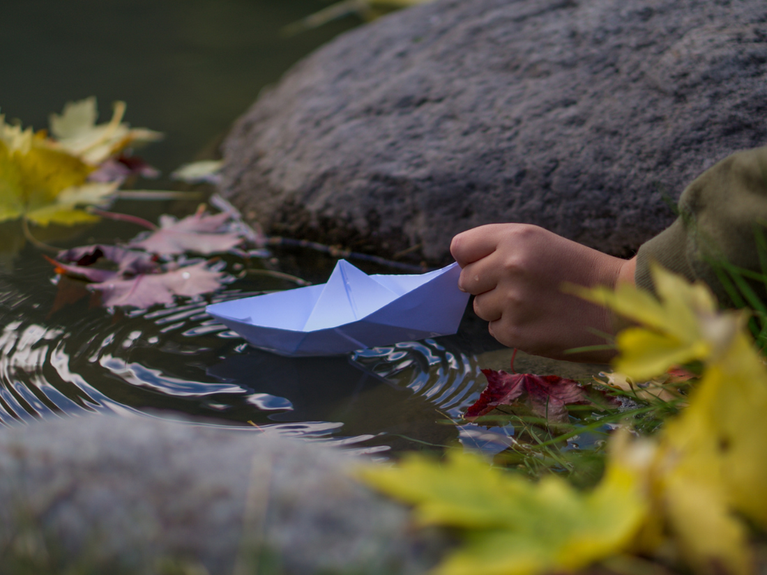 A hands releasing a paper boat into a flowing river