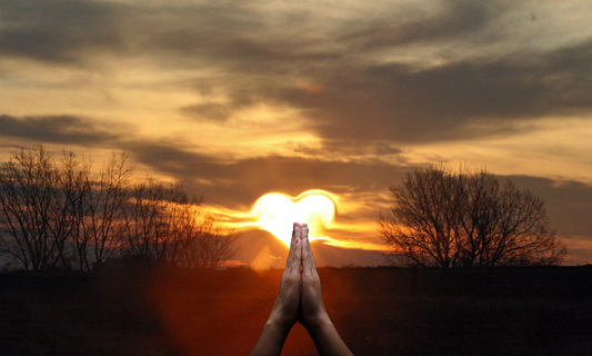 hands clasp in prayer with sunrise in the background