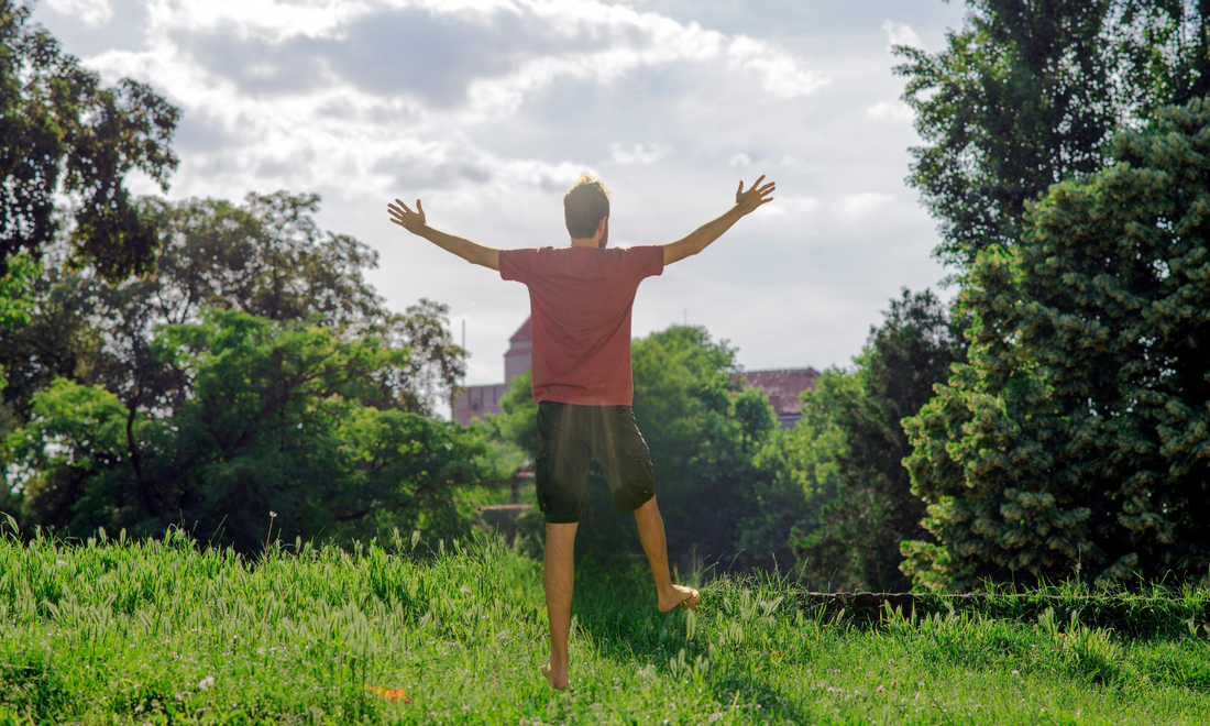 A person standing barefoot in a calm meadow at sunrise, arms open