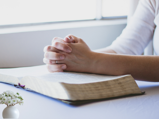open Bible and folded hands in soft light—praying through difficult conversations